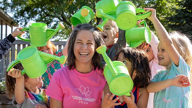 Toby surrounded by young children who are pretending to "water" her with watering cans